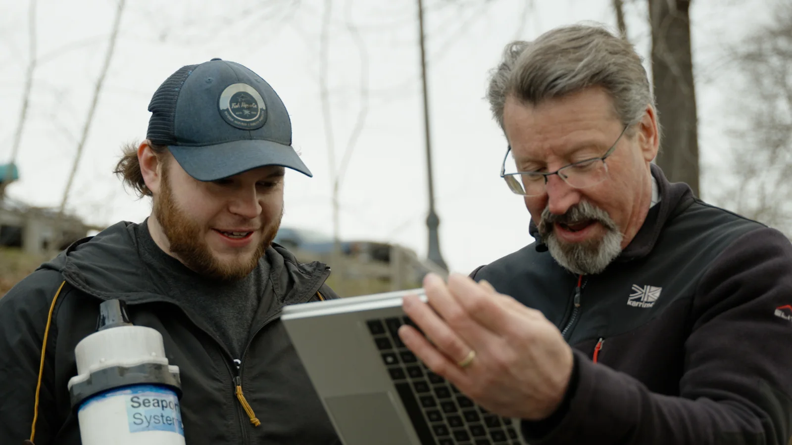 Two people reviewing sensor data on a laptop beside a Seaport Systems current meter